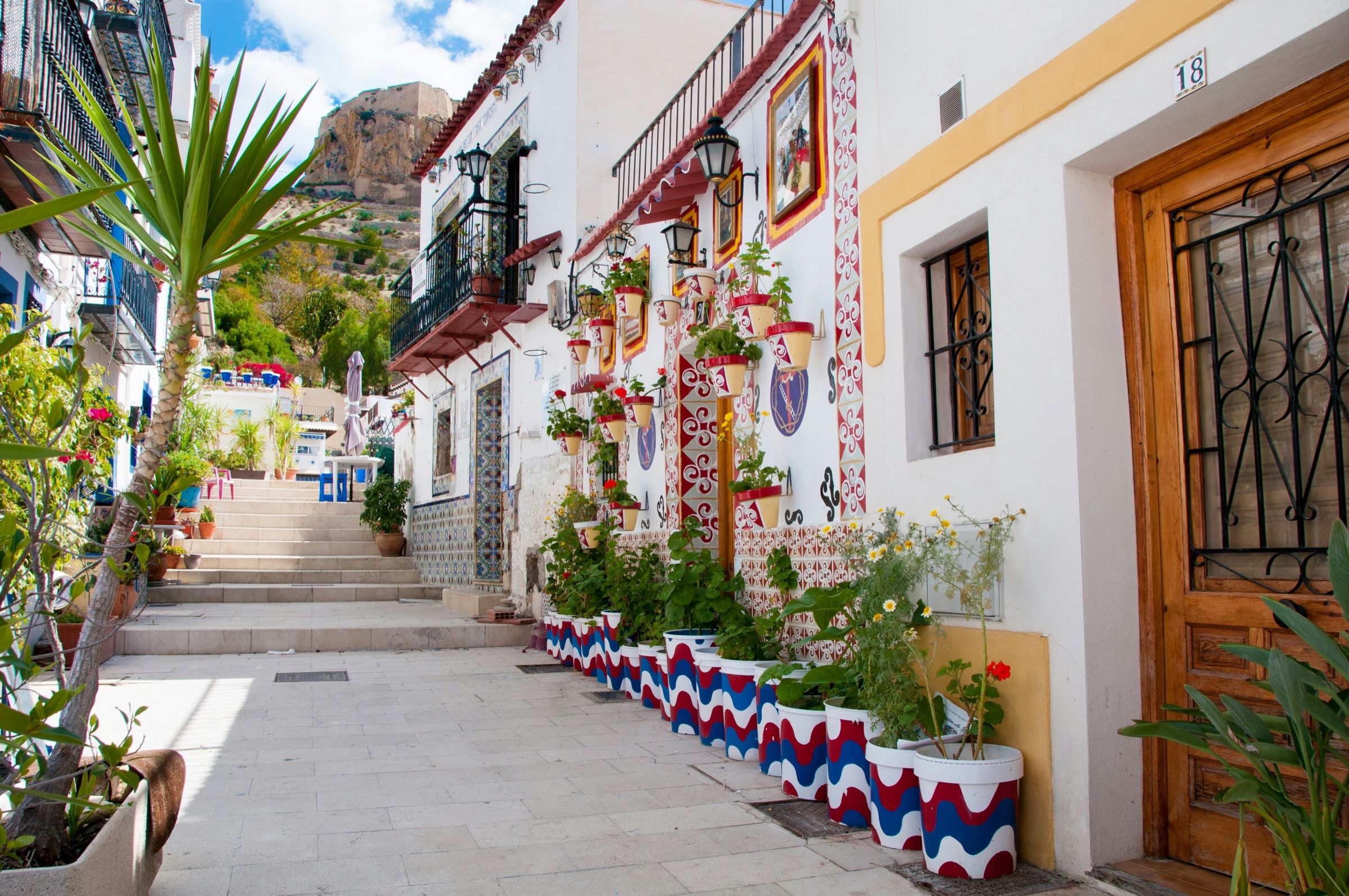 Calle del barrio de Santa Cruz, en Alicante, con macetas pintadas y el castillo de Santa Bárbara al fondo